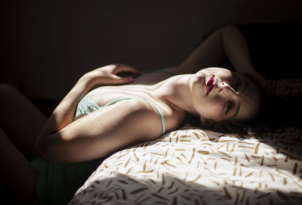 Archival print photograph by Erica McKeehen entitled "Suncatcher (from Secret Mermaid)." Woman featured laying down with her head resting on a pillow,  and light falling diagonally across the image--and on part of her face and chest.
