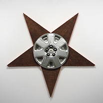 Artwork by Ryan Lucas entitled "Dying Star."  Star shaped flat wooden form with Dodge Ram hubcap in the center of the star.. It is 41.5” tall by 41.5” wide.