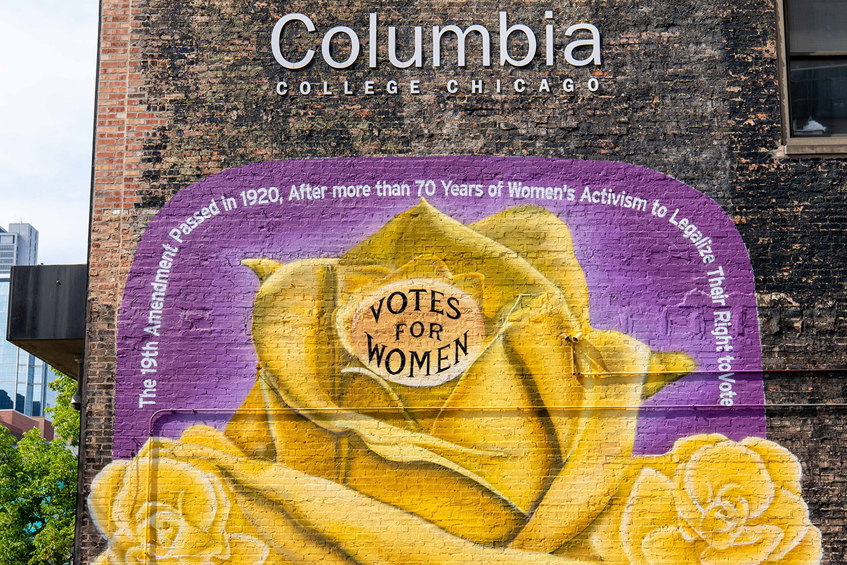 A mural on a brick building of a yellow rose with the words "Votes for women" 