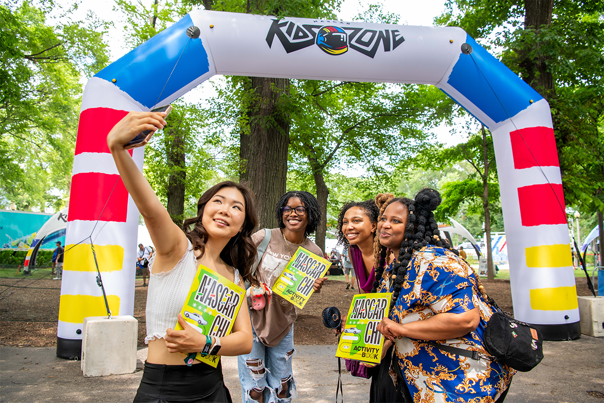 a group takes a selfie in front of blow-arch that says kidzone