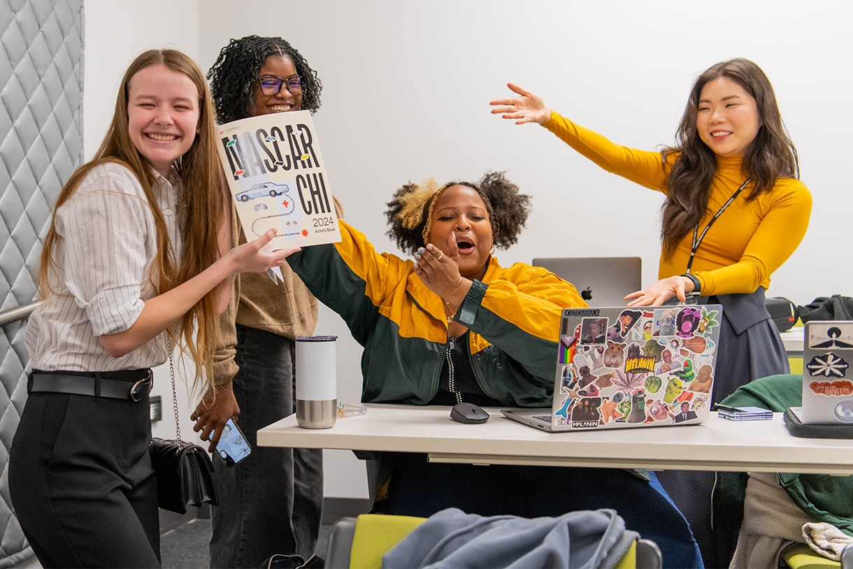 students gathered around computer and holding up a prototype of the activity booklet