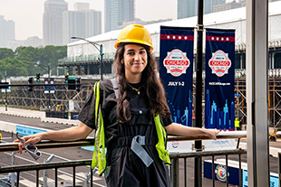 portrait of yasmine mifdal wearing hard hat with nascar race track being set up in background